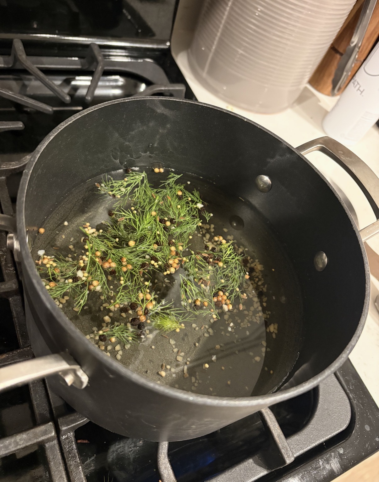 A pot of pickle brine simmering on the stove with fresh dill and spices