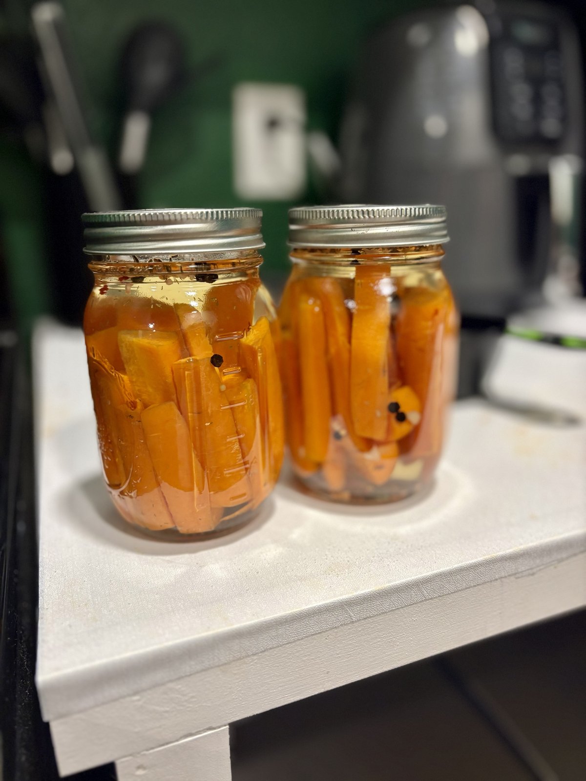 Two jars of pickled carrot spears with peppercorns and dill